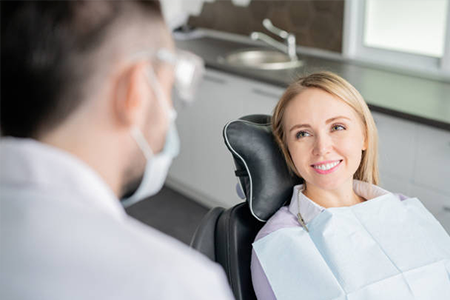 Female dentist smiling at patient in dental office chair during consultation.