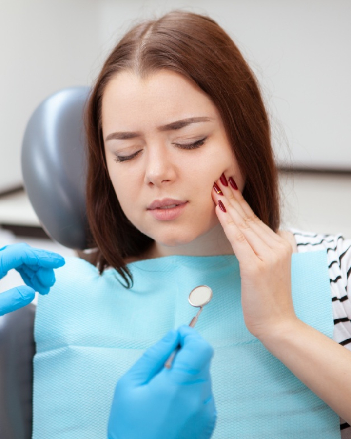 Patient experiencing tooth pain at dental office during examination by dentist in blue gloves.