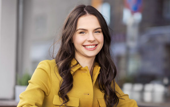 Young woman smiling at camera wearing yellow shirt in modern office setting.