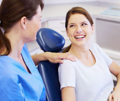 Dentist in blue scrubs showing dental chair to smiling female patient in dental office.