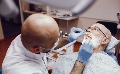 Dentist in blue gloves examining patient's teeth in dental office treatment room.