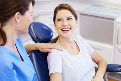 Dental professional adjusting blue headrest for smiling patient in modern dental office chair.
