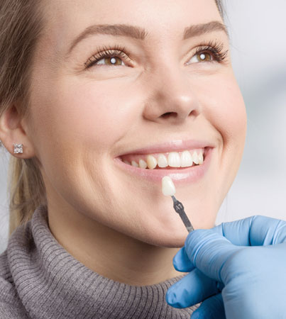 Woman receiving professional teeth shade matching during dental consultation with dentist in gloves.