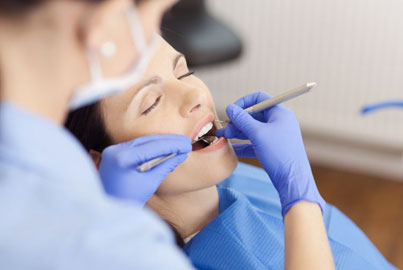 Dentist examining patient's teeth with tools in dental office setting.