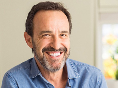 Smiling male dentist in light blue shirt against neutral indoor background.