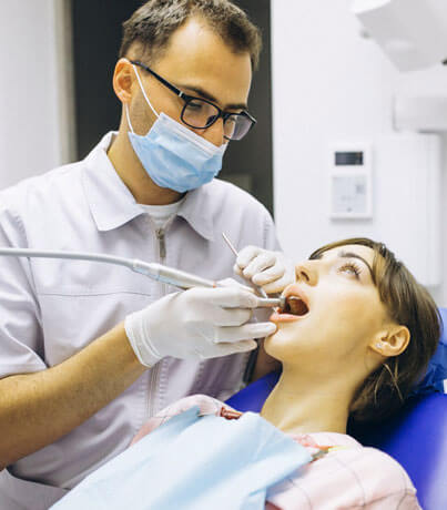 Male dentist examining female patient's teeth in dental office wearing mask and gloves.