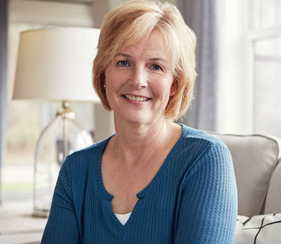 Smiling blonde woman in blue top seated indoors, professional dental office setting.