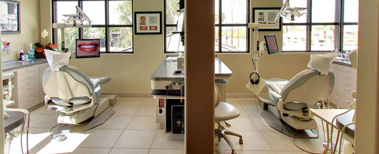 Dental operatory rooms with treatment chairs, equipment, and natural lighting in modern clinic setting.