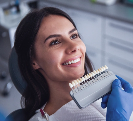 Smiling dental professional in blue gloves holding shade guide in modern dental office.
